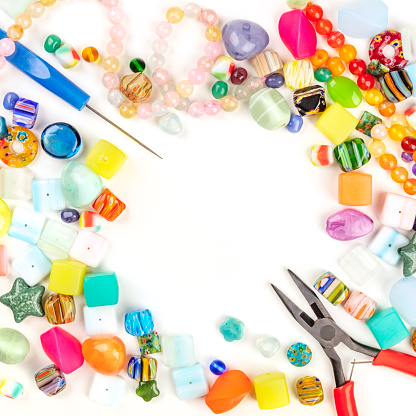 A square photo of beads with tools for making jewelry, shot from above on a white background with copyspace