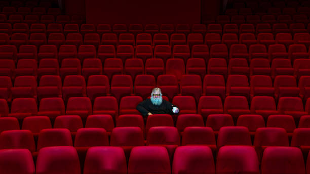 istock One man with white beard sits in Empty cinema or theatre with comfortable red seats 1154917458