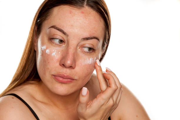istock beautiful middle-aged woman applying moisturizer on her face on white background 1154922503