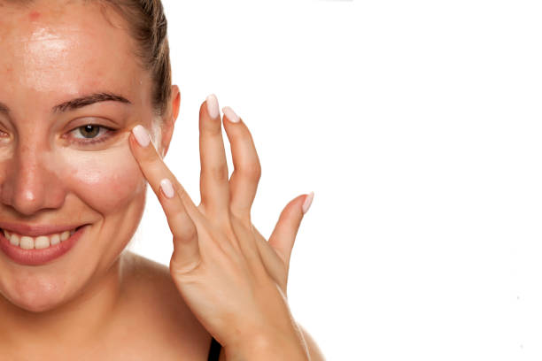 istock Young woman applying concealer under her eyes with brush on white background 1154922530