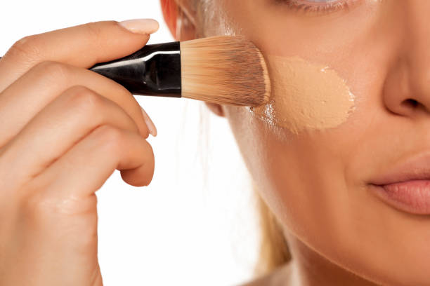 istock Young woman applying liquid foundation with brush on white background 1154922562
