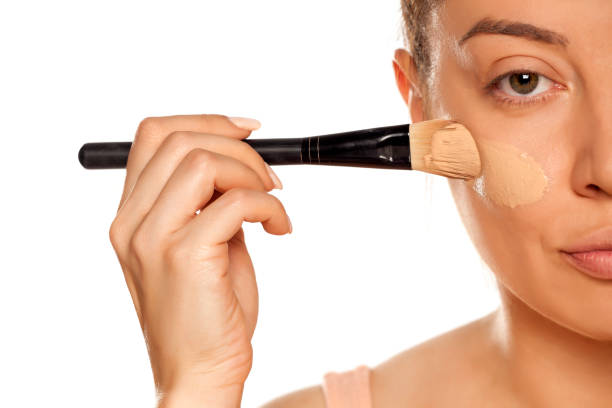 istock Young woman applying liquid foundation with brush on white background 1154922563