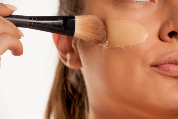 istock Young woman applying liquid foundation with brush on white background 1154922566