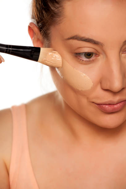 istock Young woman applying liquid foundation with brush on white background 1154922572
