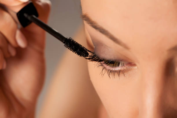 istock Young woman applying mascara on white background 1154922585