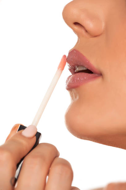 istock Young woman applying lipgloss on white background 1154923117