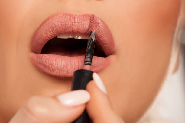 istock Young woman applying lipgloss on white background 1154923120
