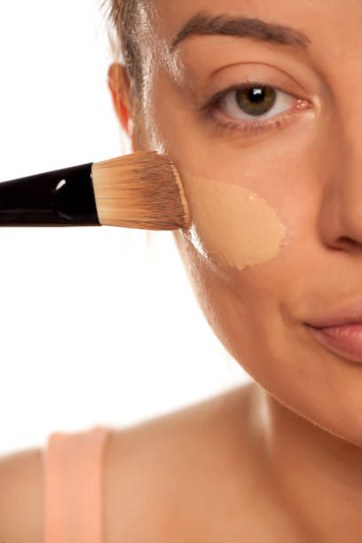 istock Young woman applying liquid foundation with brush on white background 1154923174