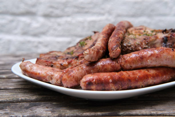 Delicious sausages, steaks on white dish over rough wooden table.