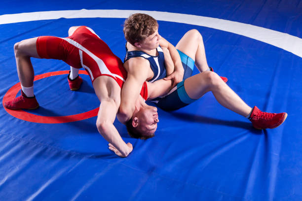 Two young sportsmens wrestlers Two young sportsmens wrestlers in red and blue uniform wrestling against wrestling carpet, view above. wrestling sport stock pictures, royalty-free photos & images