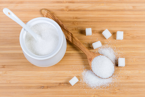 White sugar in sugar-bowl, wooden spoon and sugar cubes