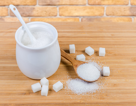 White sugar in sugar-bowl, wooden spoon and sugar cubes