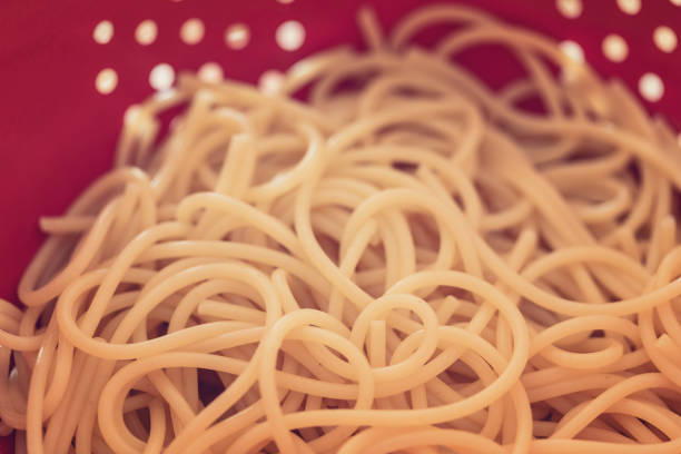 Fresh boiled spaghetti draining in metal colander, close-up