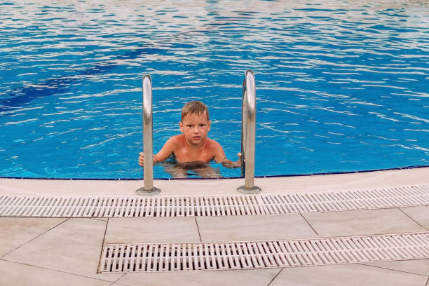 istock boy in an outdoor blue pool looking at the camera 1154942390