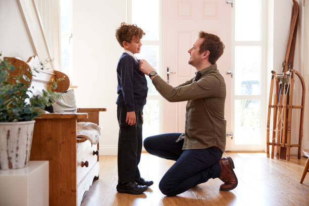 single father at home getting son wearing uniform ready for first day of school - der erste schultag stock-fotos und bilder