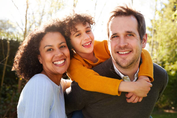 outdoor-porträt von smiling family im garten zu hause gegen flaring sun - drei personen fotos stock-fotos und bilder