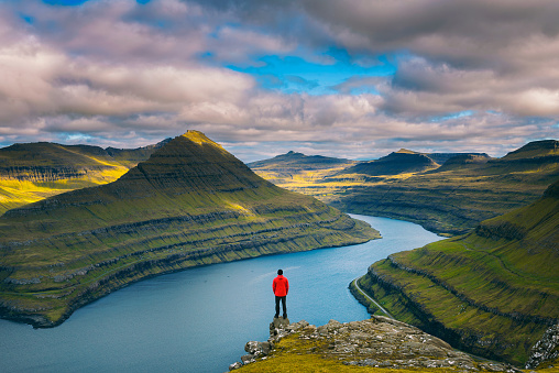 Hiker enjoys spectacular views over fjords from the summit of a mountain near Funningur on Faroe Islands.