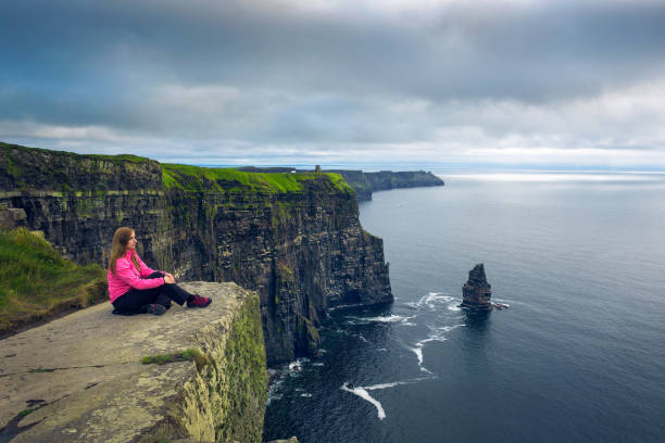 mulher nova que senta-se nos penhascos de moher - republic of ireland cliffs of moher panoramic cliff - fotografias e filmes do acervo