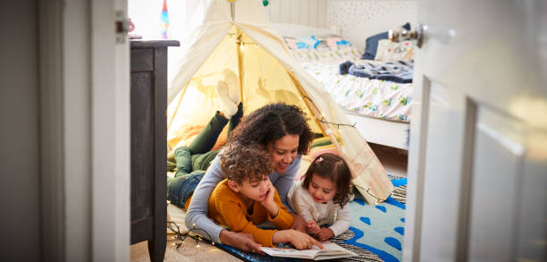 madre single che legge con figlio e figlia in tana in camera da letto a casa - child reading mother book foto e immagini stock