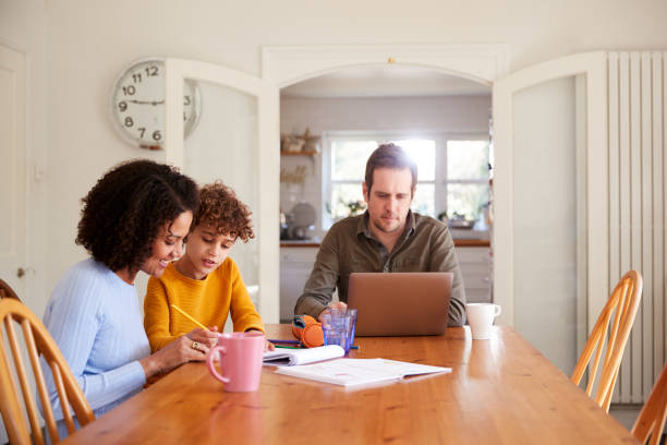 istock Father Works On Laptop As Mother Helps Son With Homework On Kitchen Table 1154944439