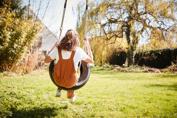 задний вид девушки весело провести время на шины качели в саду у себя дома - tire swing стоковые фото и изображения
