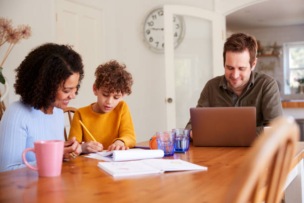 ojciec pracuje na laptopie, ponieważ matka pomaga synowi odrabiać lekcje na kuchennym stole - homework child mother parent zdjęcia i obrazy z banku zdjęć