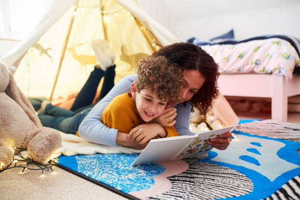 single mother reading with son in den in bedroom at home - child reading mother book imagens e fotografias de stock