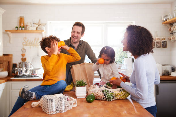 famille rentrant à la maison du shopping voyage utilisant des sacs gratuits en plastique déballant l’épicerie dans la cuisine - two parent family indoors home interior domestic kitchen photos et images de collection