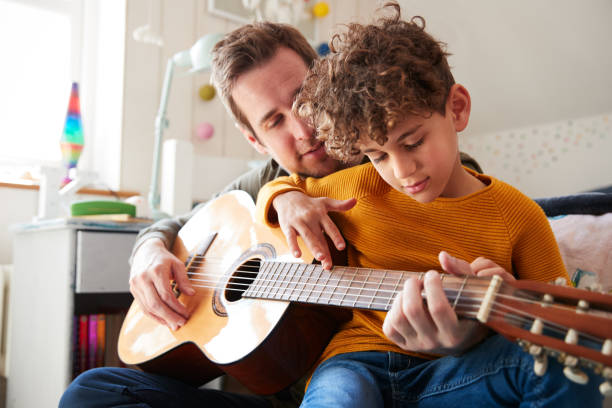 père célibataire à la maison avec fils lui apprenant à jouer la guitare acoustique dans la chambre à coucher - guitar child music learning photos et images de collection