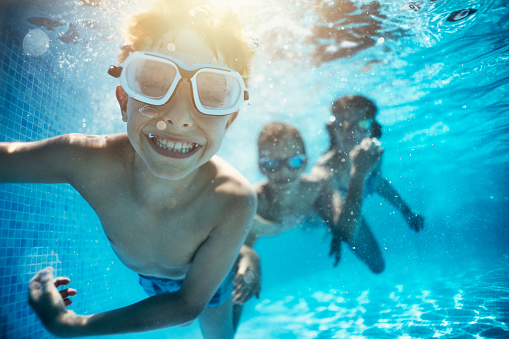 Happy kids having underwater party in the swimming pool. The boy is grinning at the camera. \nShot with Nikon D850.