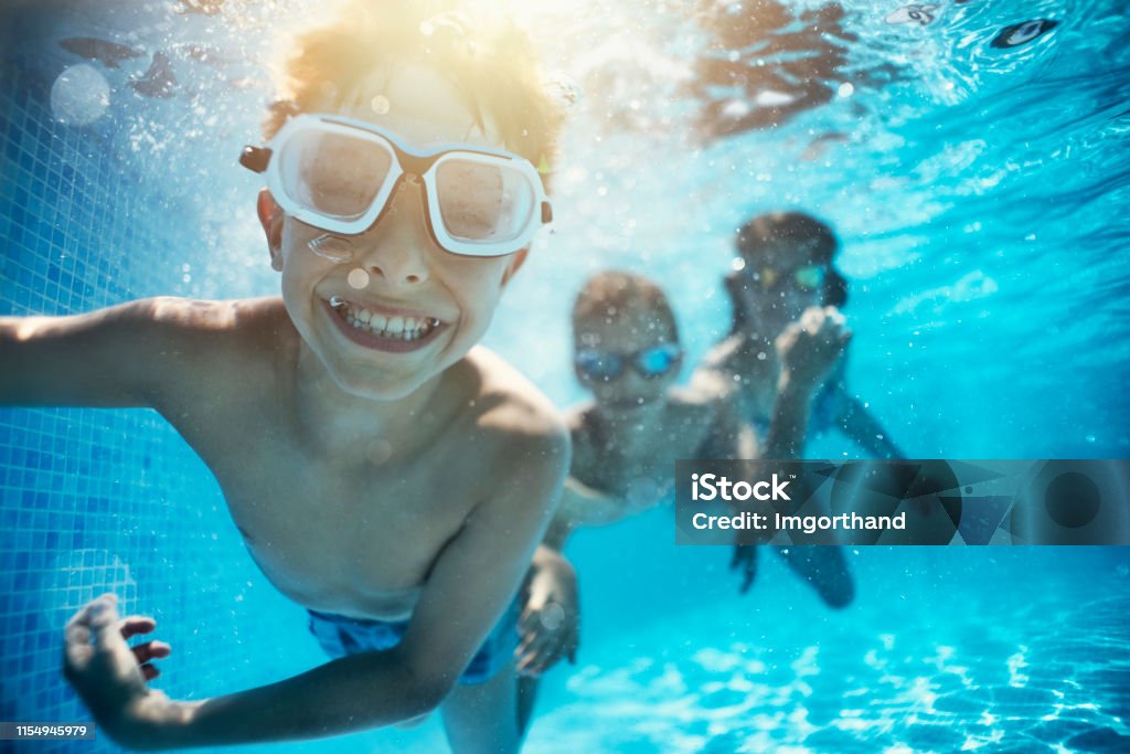 Kids playing underwater in pool Happy kids having underwater party in the swimming pool. The boy is grinning at the camera. 
Shot with Nikon D850. Swimming Pool Stock Photo