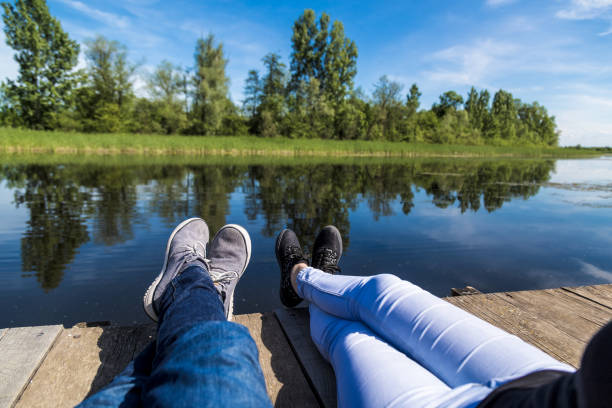 Couple sitting on pier against beautiful nature. Feet close up.