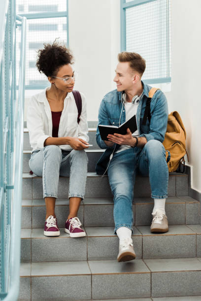 istock two multiethinc students with notebook sitting on stairs in university 1154947782