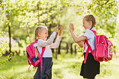 two little girls schoolgirl with pink backpack and play Patty-cake outdoors