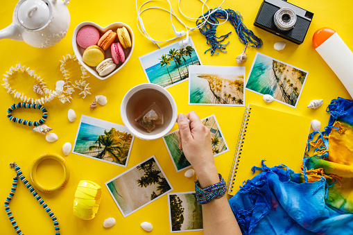 Top view of photos from summer vacations and personal accessories on yellow background.