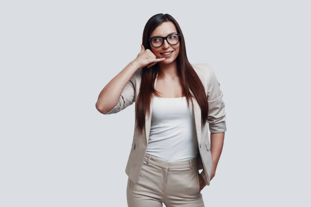 istock Give me a call! Attractive young woman gesturing and smiling while standing against grey background 1154954556