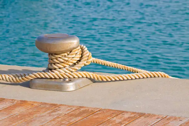 Cleat for mooring boats on wooden platform against a water with a rope