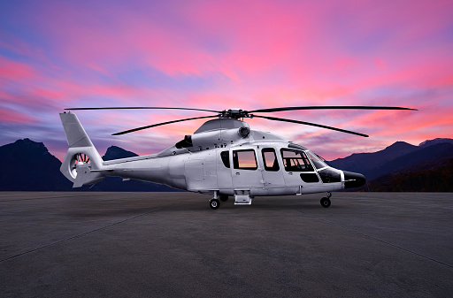 Silver helicopter on parking apron at sunset in dramatic sky.
