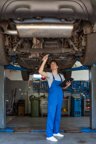 Double-checking the steering column Photo of a mechanic at work in his garage. Male Mechanic with clipboard examining under a car in the workshop. Car service, repair, maintenance and people concept - happy smiling auto mechanic man or Smith with a clipboard at the workshop, looking up. mechanic working under car stock pictures, royalty-free photos & images