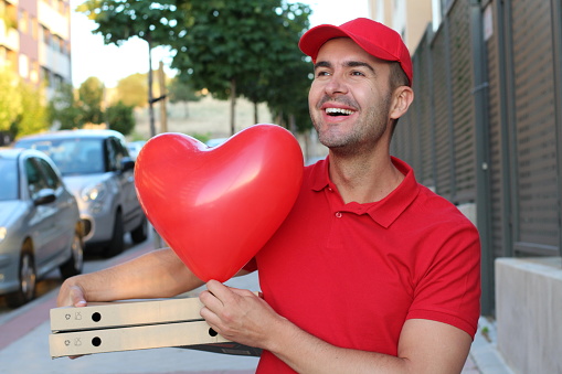 Cute pizza delivery guy holding pizzas and heart shaped balloon.