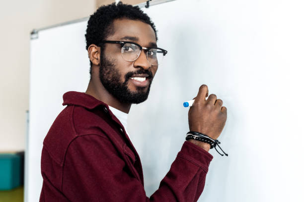 istock smiling african american student in glasses writing on flipchart 1154963651