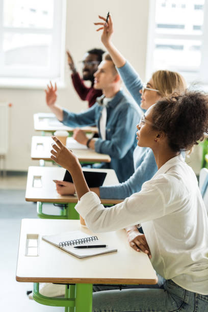 istock selective focus of multiethnic students sitting at desks and raising hands 1154963719