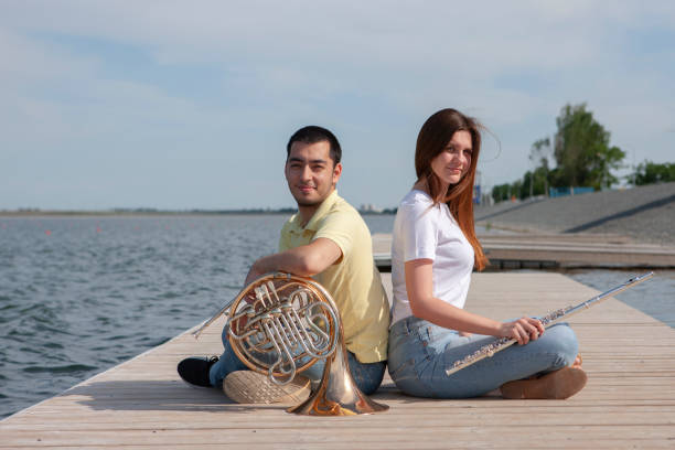 il ragazzo che suona il corno e la ragazza che suona il flauto sul lago - musical instrument close up wind instrument brass instrument foto e immagini stock