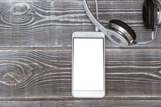 istock Phone with a white blank screen and headphones on a wooden table. 1154973251
