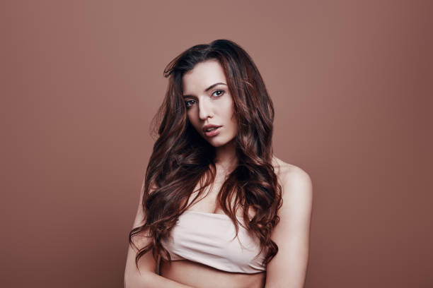 istock Enjoying her beauty. Attractive young woman looking at camera while standing against grey background 1154973320
