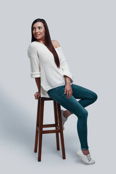 istock Feeling happy. Attractive young woman looking away and smiling while sitting against grey background 1154973450