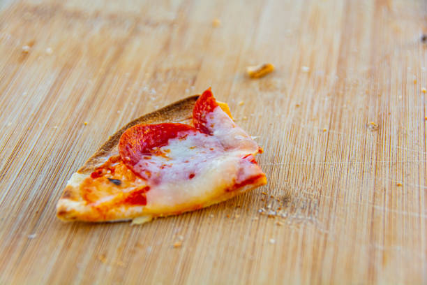One small slice of pizza and crumbs on wood cutting board
