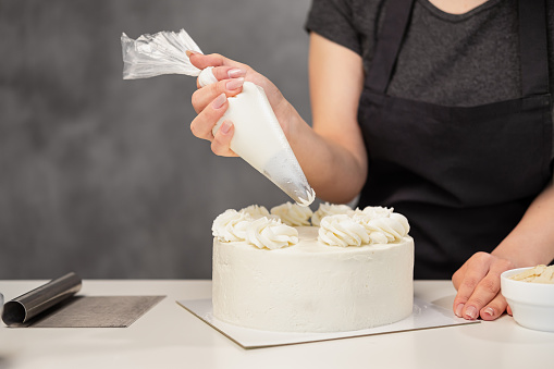 Confectioner at work. Cream cake decorating. Cook table preparing a cake on a gray background.