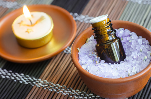 Small bottle of essential oil in the bowl with aroma bath salt and burning candle. Aromatherapy, spa and herbal medicine concept. Close up, copy space