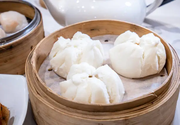 Photo of Delicious dim sum, famous cantonese food in asia - Fresh and hot Cha Siu Bao, BBQ pork bun in bamboo steamer in hong kong yumcha restaurant, close up